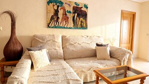 Un soggiorno con divano, tavolino in vetro, un comodino in legno, un vaso e un quadro appeso al muro.