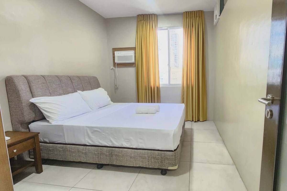 Une chambre d’hôtel avec un lit, une table de chevet, une fenêtre avec des rideaux et une porte.
