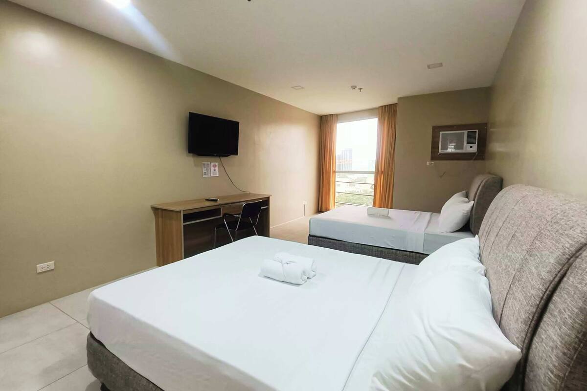 Une chambre d’hôtel avec deux lits, un bureau, une chaise, une télévision et une fenêtre avec des rideaux.