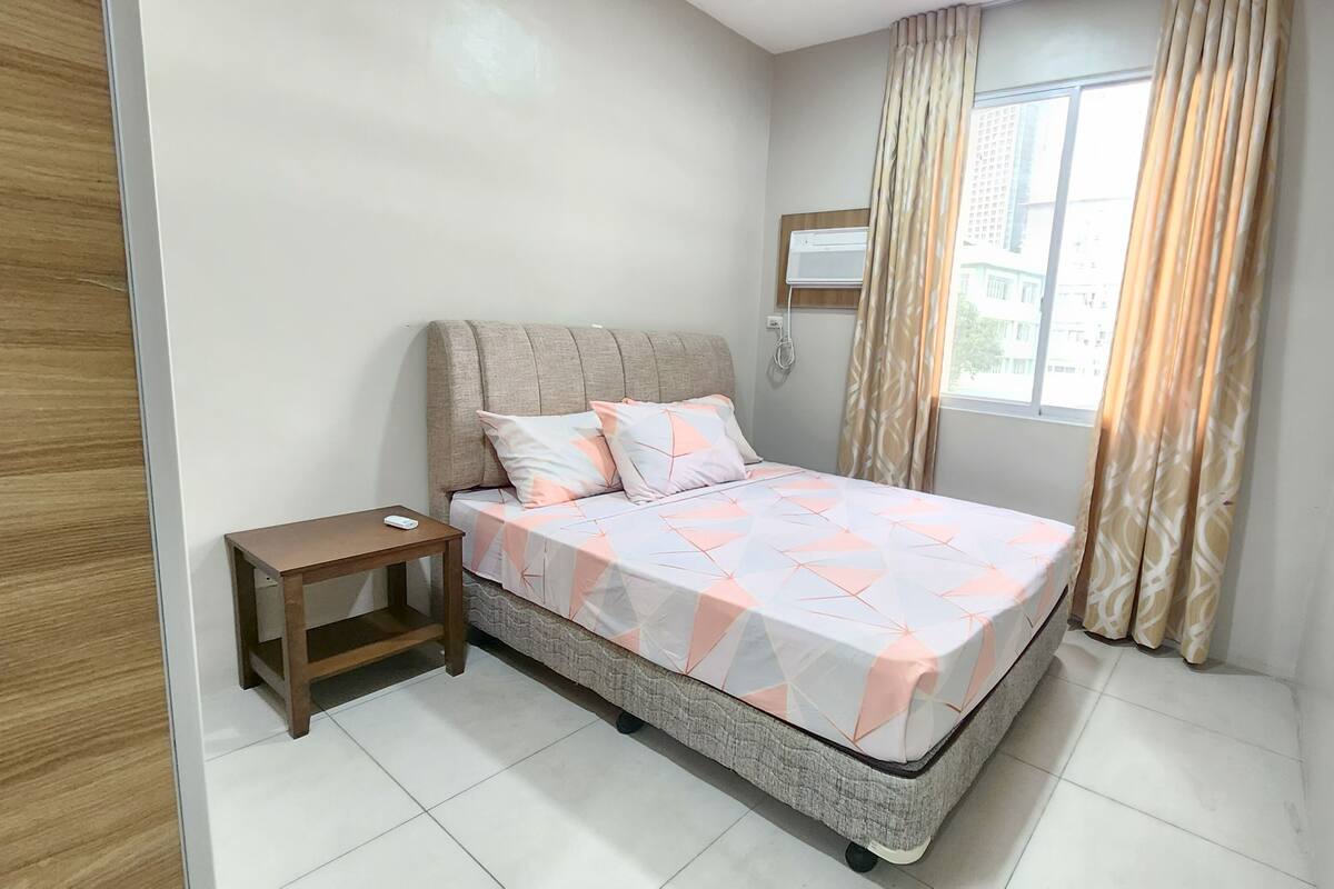 Une chambre à coucher comprenant un lit, une table de chevet, une fenêtre avec des rideaux et un climatiseur fixé au mur.
