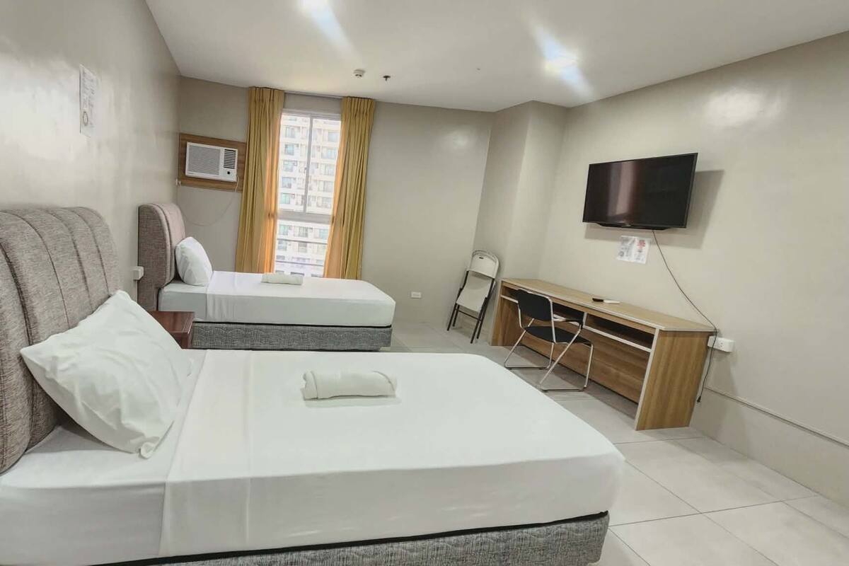 Une chambre d’hôtel avec deux lits, un bureau, une chaise, une télévision et une fenêtre avec des rideaux.