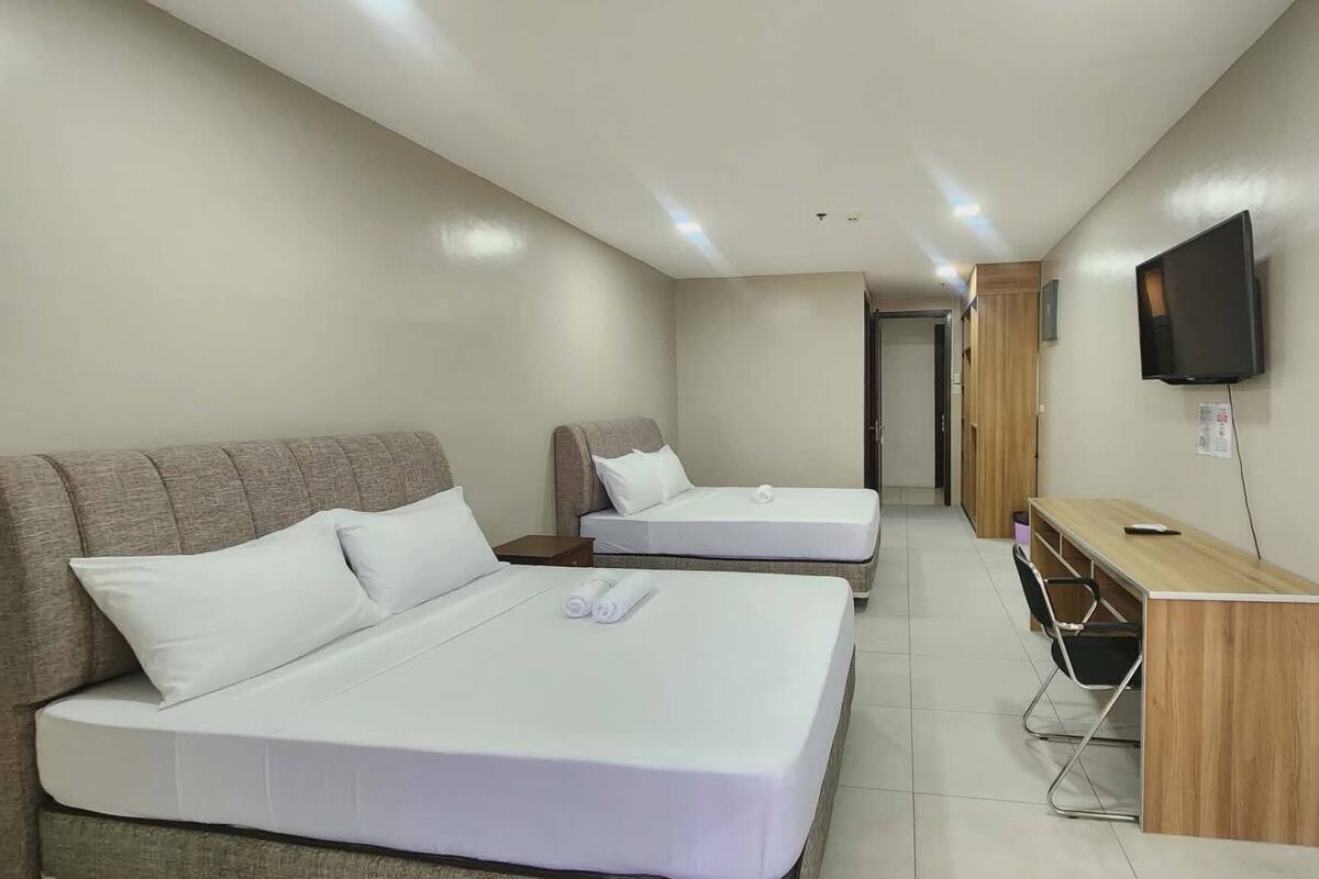 Une chambre d’hôtel avec deux lits, un bureau, une chaise, une télévision et une porte donnant sur une autre pièce.