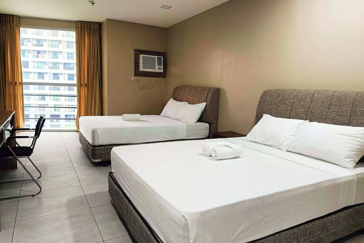 Une chambre d’hôtel avec deux lits, une chaise, une fenêtre avec des rideaux et un appareil de climatisation fixé au mur.