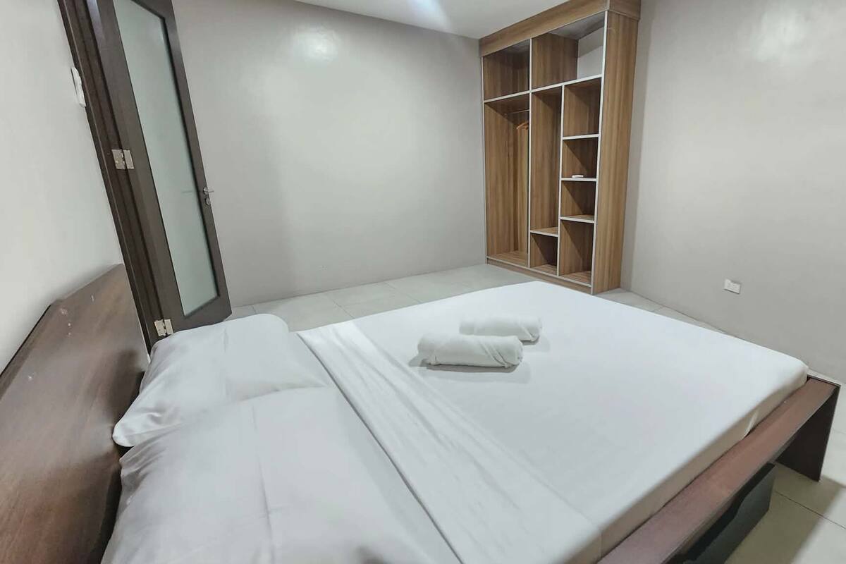 Un lit bien fait, avec du linge de lit et des serviettes blanches, une armoire en bois dotée de plusieurs étagères et un miroir accroché au mur.