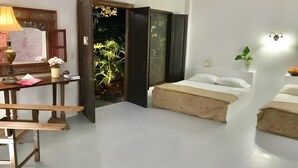 Ein Schlafzimmer mit Bett, Nachttisch, Lampe und Blick auf einen Garten durch eine offene Tür.