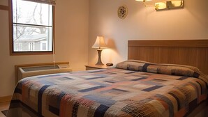 Una camera da letto con un letto grande, un comodino con una lampada, una finestra con persiane e un punto luce a parete.
