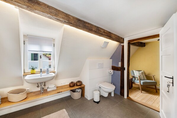 A modern bathroom with a sink, toilet, and a wooden bench.