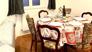 A dining area with a table set for four, a window with curtains, and a painting on the wall. - Apartment at Suzannala 5 minutes from Colmar 6 people (Ingersheim)