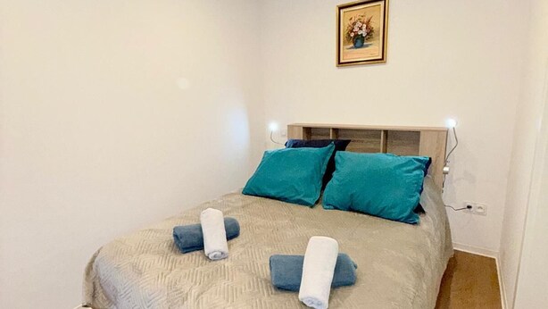 A neatly made bed with a patterned bedspread and two pillows, a small framed picture on the wall, and a bedside table with a lamp. - Apartment at Suzannala 5 minutes from Colmar 6 people (Ingersheim)