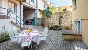 An outdoor dining area with a table set for two, surrounded by white metal chairs. - Apartment at Suzannala 5 minutes from Colmar 6 people (Ingersheim)