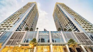 A modern high-rise building with two towers, featuring a glass facade and a central entrance with signage. - Vogue | Damac Maison Prive Downtown Near Dubai Mall | Burj Khalifa (Dubai)