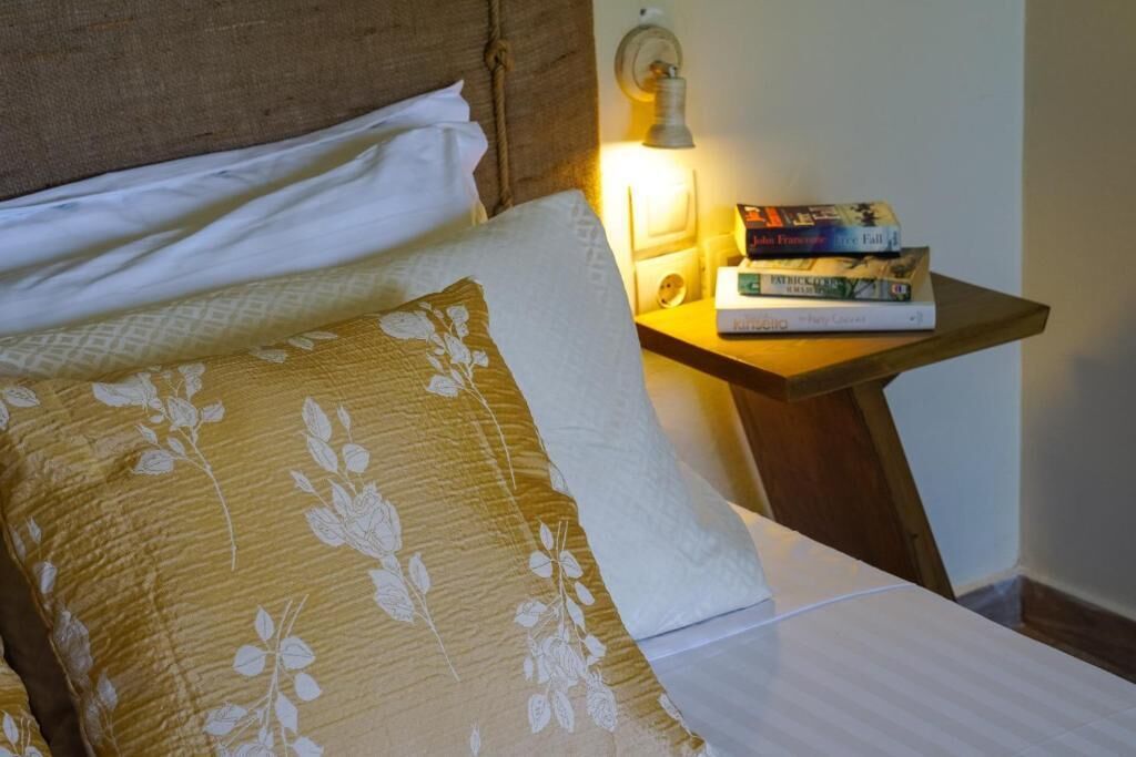 A neatly made bed with floral-patterned pillows, a bedside table with a lamp, and a stack of books.