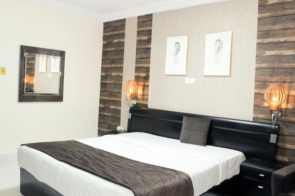 Habitación de hotel con una cama grande, un revestimiento de madera, dos obras de arte enmarcadas y lámparas de noche.