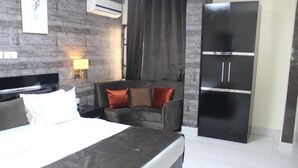 A hotel room with a bed, a chair, a wardrobe, and a wall-mounted air conditioner. - Oxygen Orbis Hotel (Ibadan)