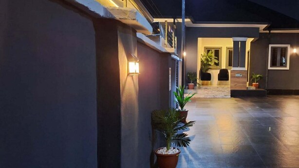 A nighttime view of a building's exterior with a paved walkway, potted plants, and outdoor seating area. - Oxygen Orbis Hotel (Ibadan)