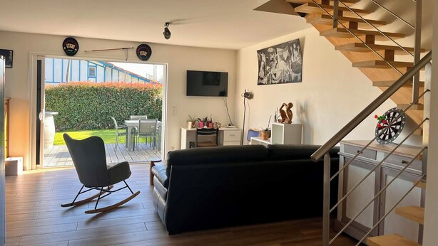 Un salon moderne avec un escalier, un téléviseur et un coin repas visible à travers une porte vitrée.