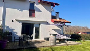 Un bâtiment blanc avec un toit recouvert de tuiles rouges, une porte-fenêtre coulissante et un patio aménagé avec du mobilier d’extérieur.