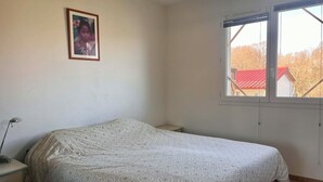 Une chambre à coucher avec un lit, un bureau, une chaise, une fenêtre et un tableau encadré au mur.