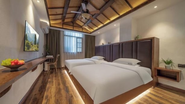 A hotel room with a wooden ceiling, a bed with white bedding, a desk with a bowl of fruit, and a painting on the wall.