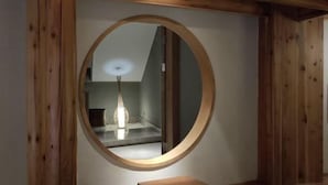 A circular mirror with a wooden frame, reflecting a room with a vase and a table.