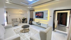 A modern living room with a flat-screen TV mounted on the wall, a coffee table, and seating area. - SGI APARTMENT (Abuja)