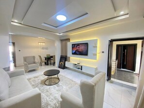 A modern living room with a flat-screen TV mounted on the wall, a coffee table, and seating area. - SGI APARTMENT (Abuja)