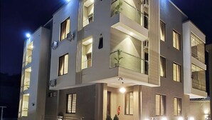 A modern multi-story building with balconies, large windows, and a well-lit entrance. - SGI APARTMENT (Abuja)