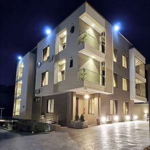 A modern multi-story building with balconies and a well-lit entrance. - SGI APARTMENT (Abuja)