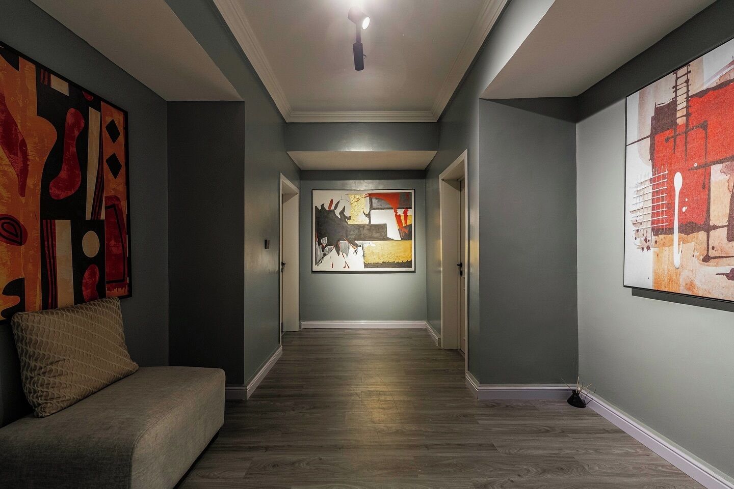 A hallway with a couch, wooden flooring, and abstract art on the walls.