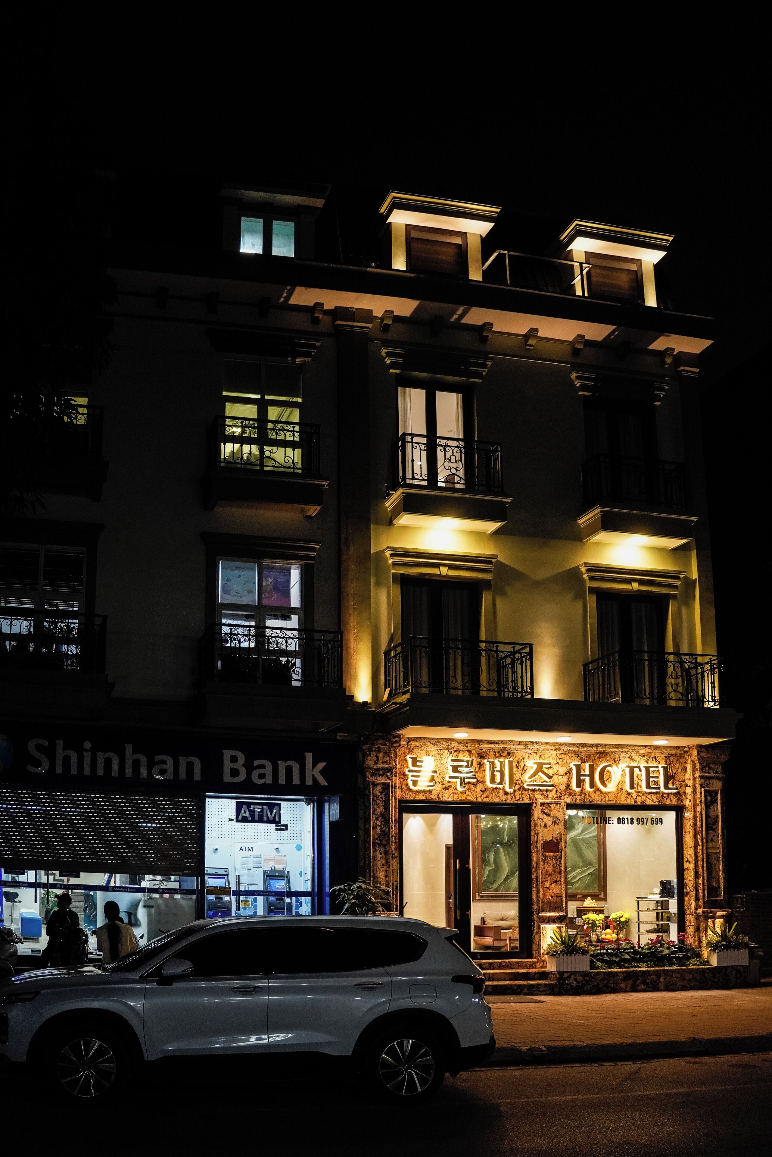 Et hotel med en moderne facade, en synlig pengeautomat og en hvid bil foran.