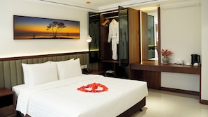 Habitación de hotel con cama, mesita de noche, escritorio con silla, bata colgada en la puerta y un cuadro en la pared.