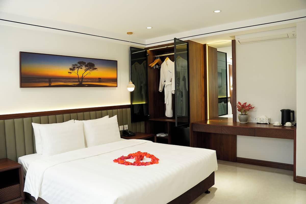 Habitación de hotel con cama, mesita de noche, escritorio con silla, bata colgada en la puerta y un cuadro en la pared.