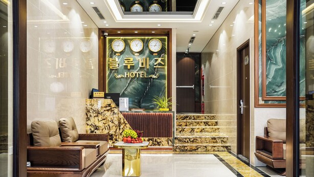 Un vestíbulo de hotel con mostrador de recepción, un área de descanso y una escalera que conduce al piso superior.