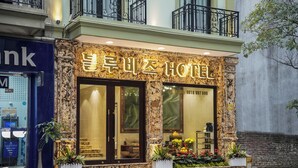 Un hotel con fachada de mármol, ventanas amplias y un balcón con barandilla de hierro forjado.