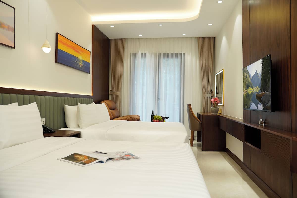 Habitación de hotel con dos camas, un escritorio, una silla, un televisor y un amplio ventanal con cortinas.