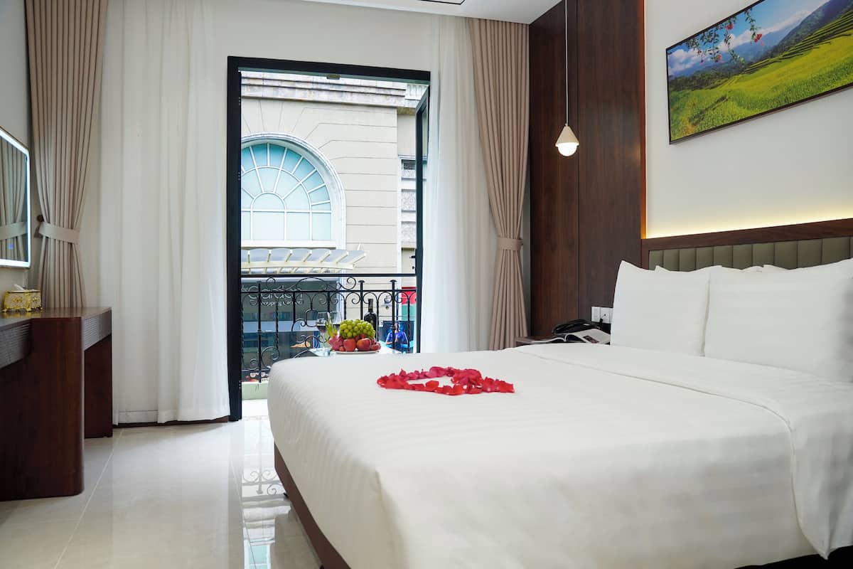 Habitación de hotel con una cama grande, un escritorio, vistas a un balcón con barandilla y un cuadro en la pared.