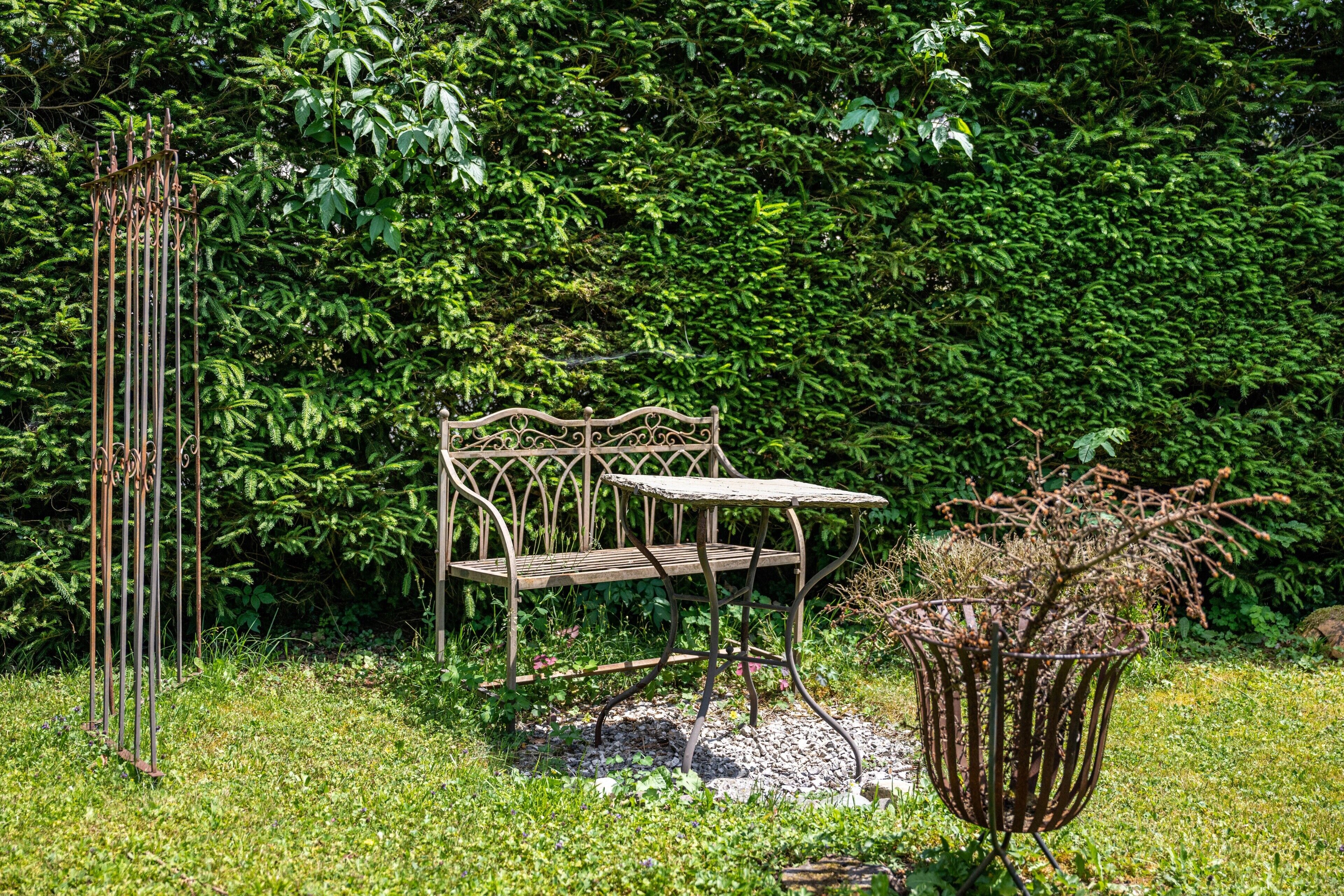 A garden with a metal bench, a metal sculpture, and a metal planter with plants.