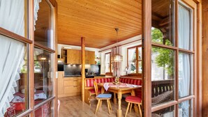 Interior de uma cabana de madeira com área de refeições, cozinha e grandes janelas.