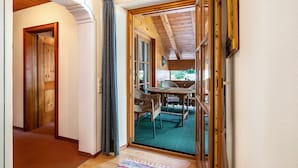 Um corredor que leva a uma sala de jantar com uma mesa e cadeiras, vigas de madeira no teto e uma porta com cortina.
