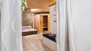 Quarto com teto de madeira, cama com colcha estampada, guarda-roupa de madeira e uma pequena mesa com revistas.