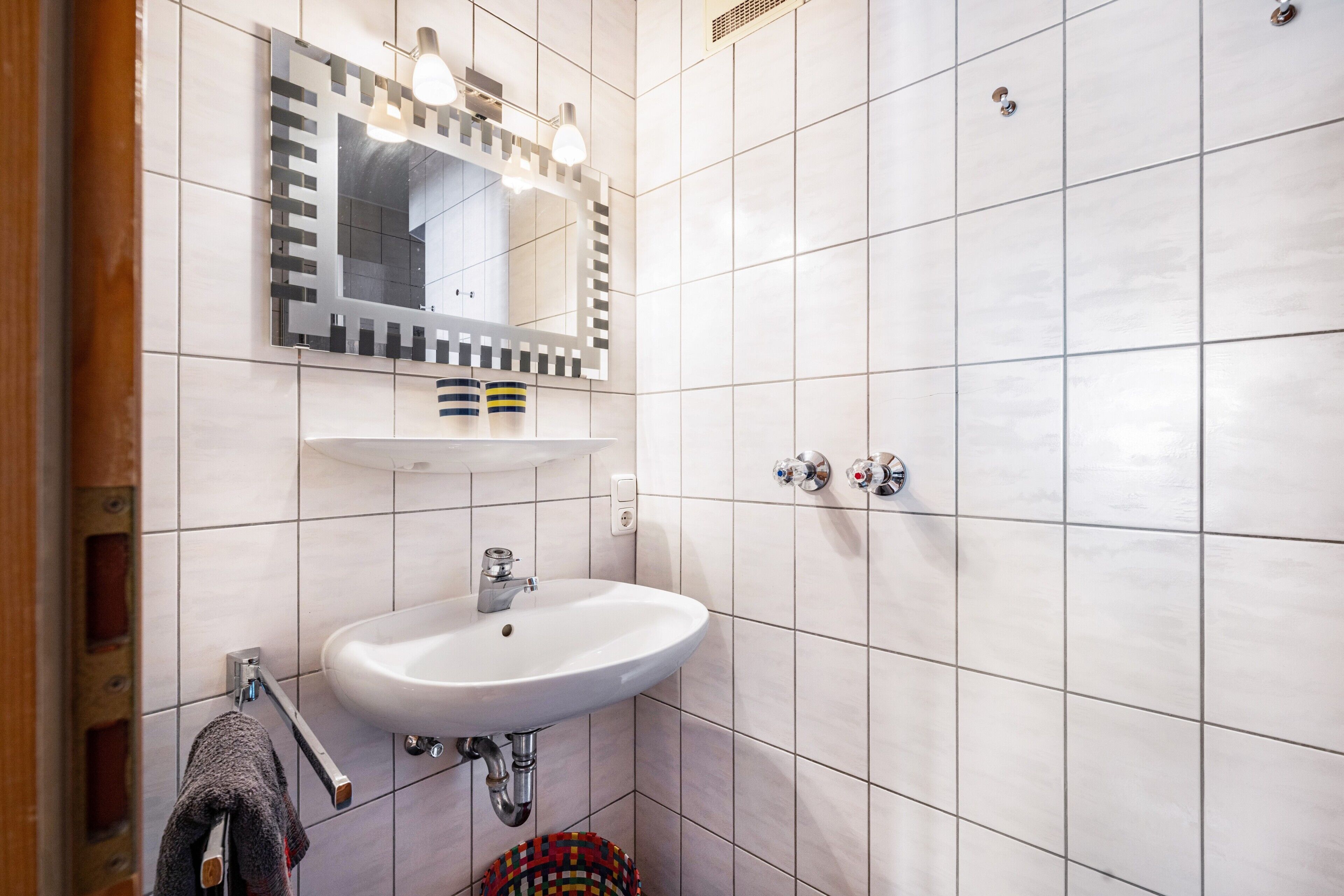 Ein Badezimmer mit einem weißen Waschbecken, einem Spiegel mit Beleuchtung und einem Handtuchhalter.