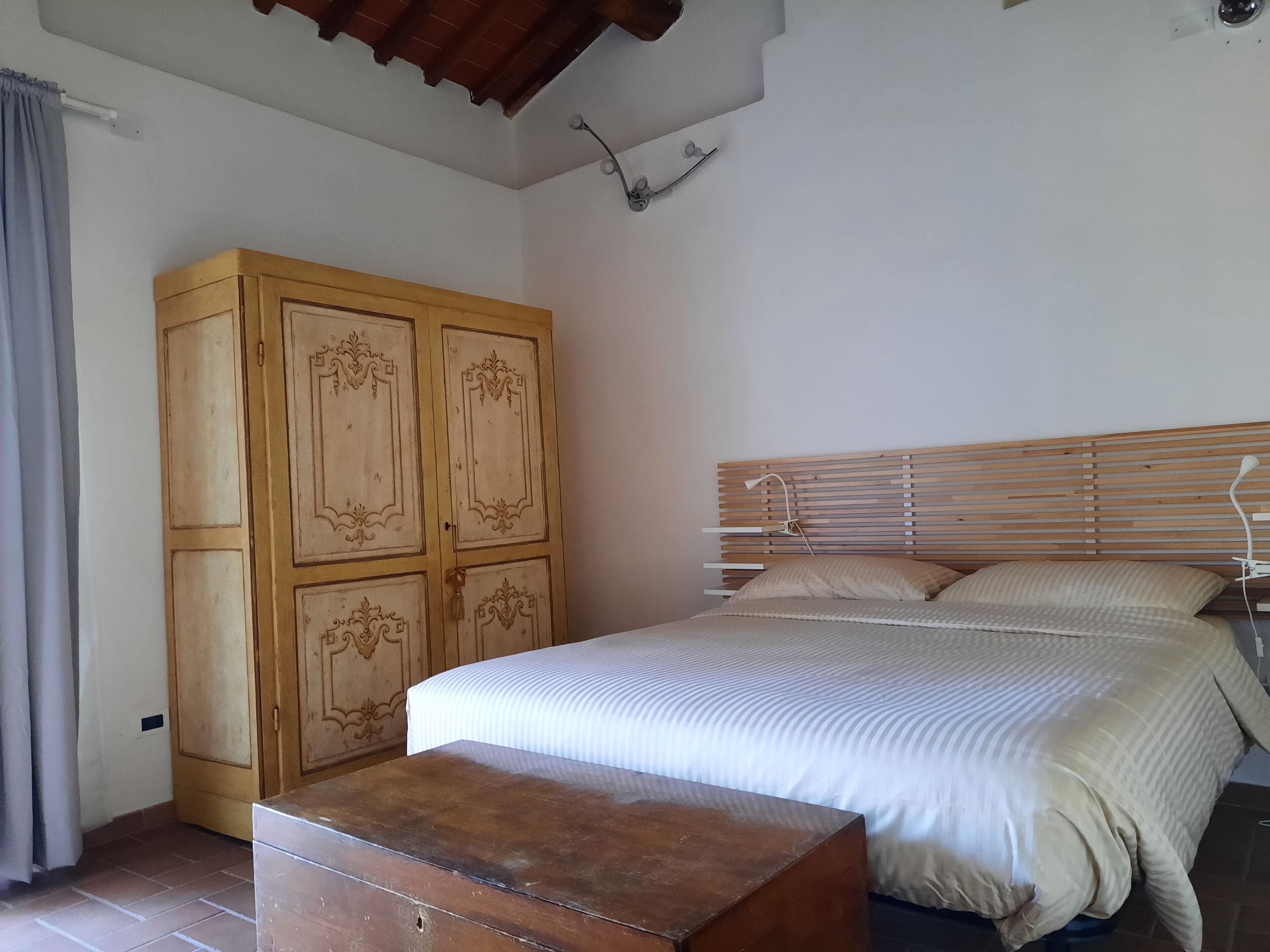 A bedroom with a wooden wardrobe, a bed with a headboard, and a bedside table.