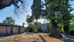 Un bâtiment rustique en pierre, doté d’une cheminée, entouré d’arbres et d’une zone herbeuse aride.