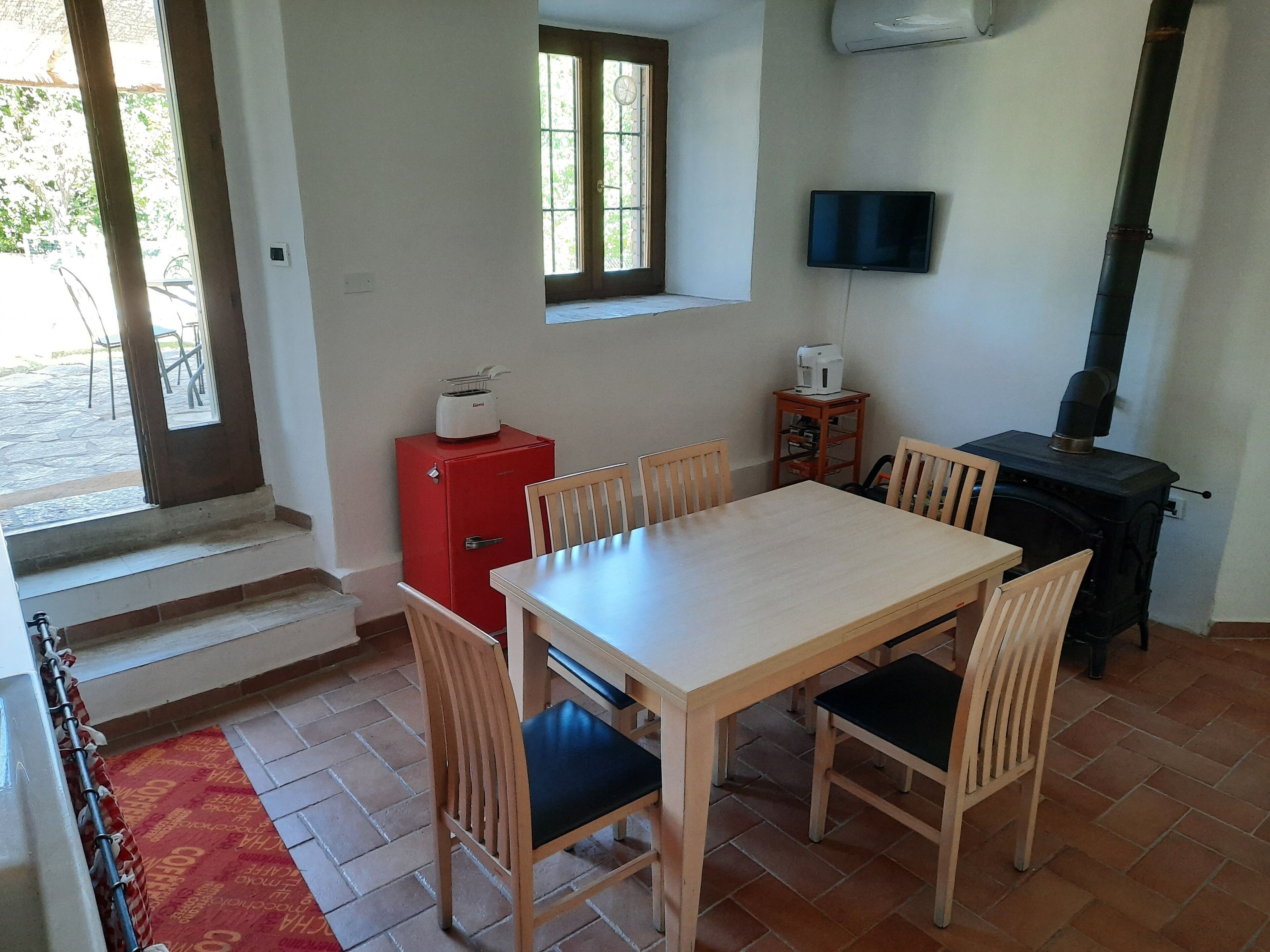 A dining area with a table and chairs, a red refrigerator, a television, and a wood-burning stove.