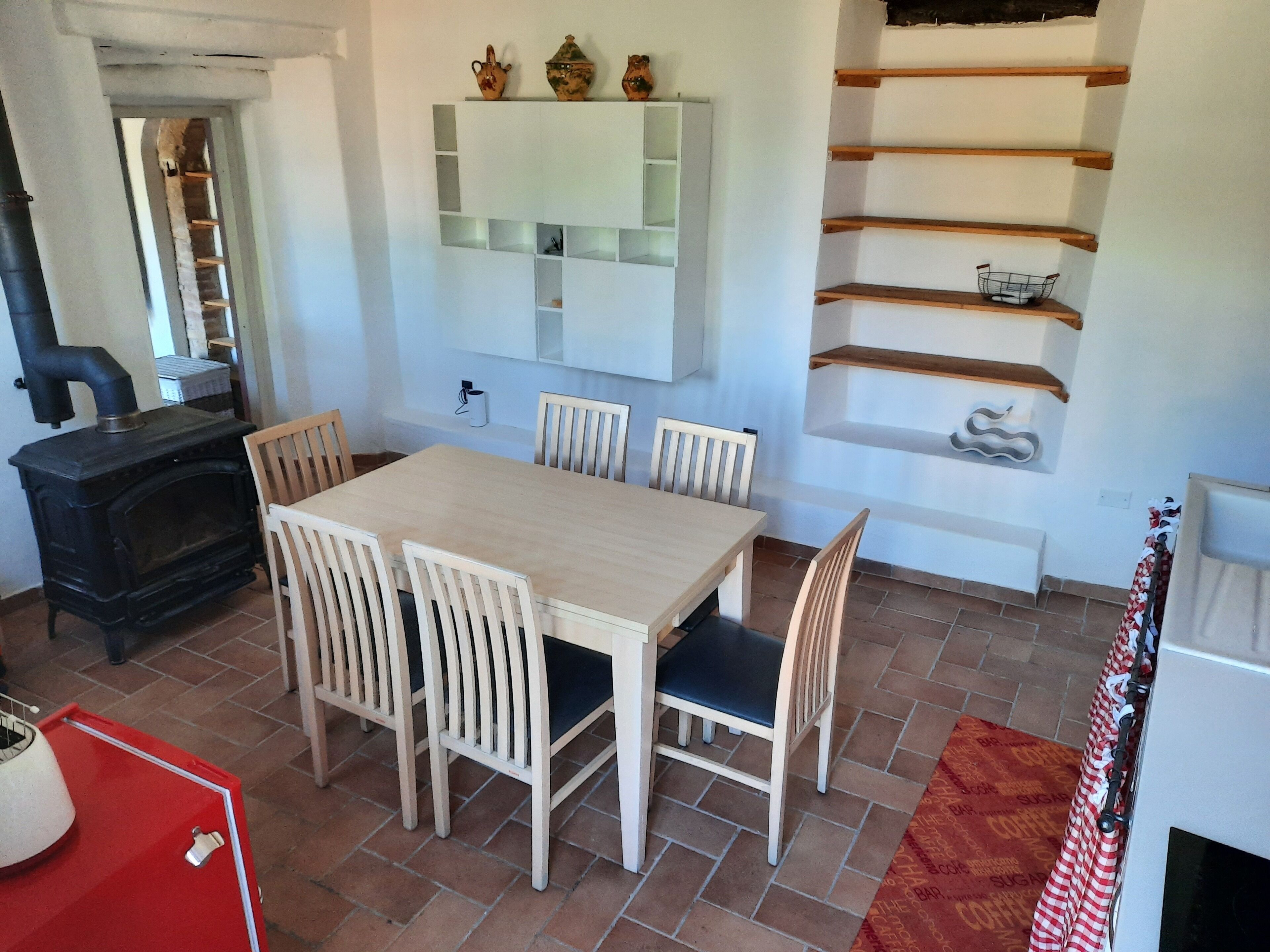 A dining area with a wooden table and chairs, a built-in shelf with decorative items, and a fireplace.