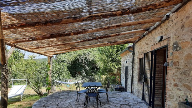 Une terrasse en pierre avec une table et des chaises, un hamac suspendu et un bâtiment en pierre doté d’une porte et d’une fenêtre.