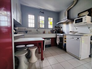 A compact kitchen with a white countertop, a stove, a microwave, and a dishwasher. There are two windows providing natural light. - Large 16-person house between Bassin d'Arcachon & Ocean, hidden from view (Lège-Cap-Ferret)