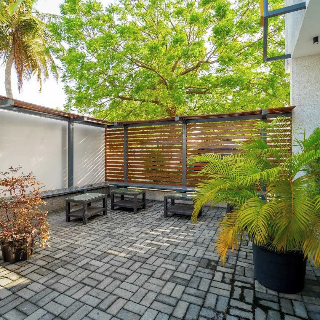A patio area with a brick floor, wooden benches, a metal fence, and potted plants.