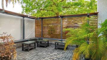 A patio area with a brick floor, wooden benches, a metal fence, and potted plants.