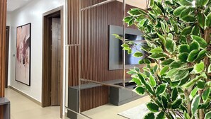 A modern hallway with a wooden panel wall, a mounted TV, and a potted plant. - THE NOOKHOUSE (Calabar)